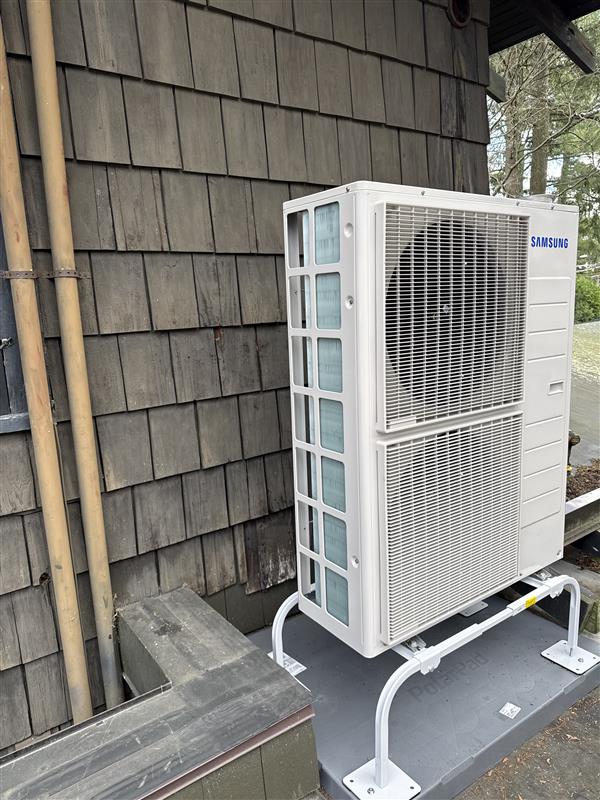 Samsung cold-climate heat pump mounted on a stand beside a shingled Upstate home